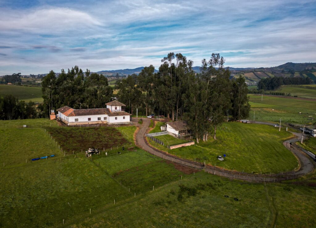 Scenic aerial shot of countryside farm with green fields and distant hills under a cloudy sky.